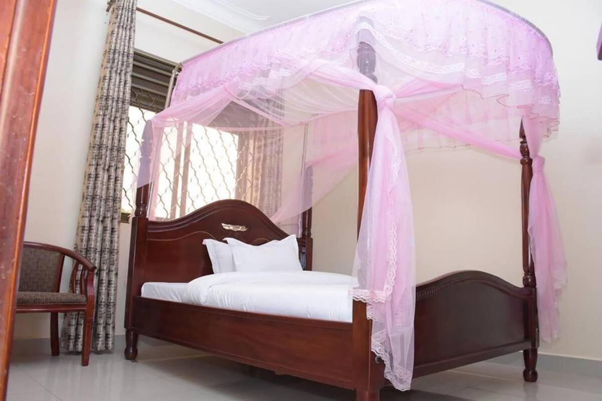 A four-poster bed with a canopy, a wooden headboard, and a white mattress.