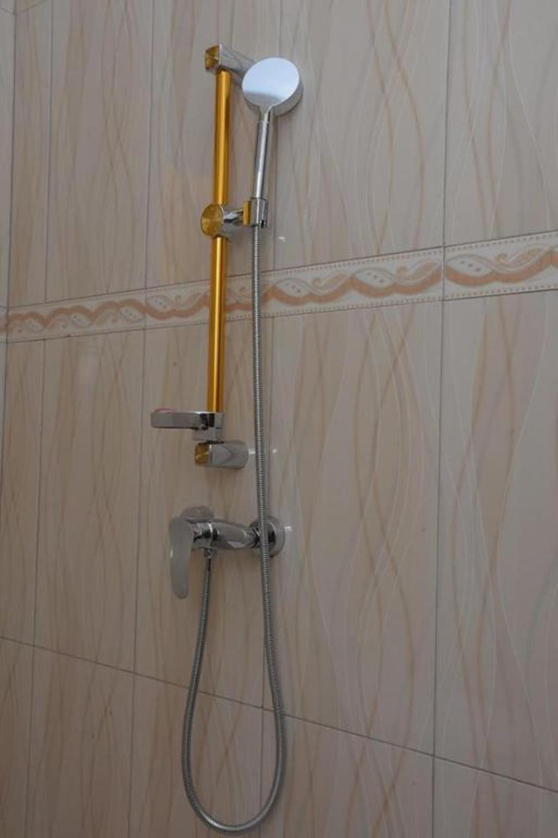 A shower with a gold handle and a white showerhead mounted on a tiled wall.