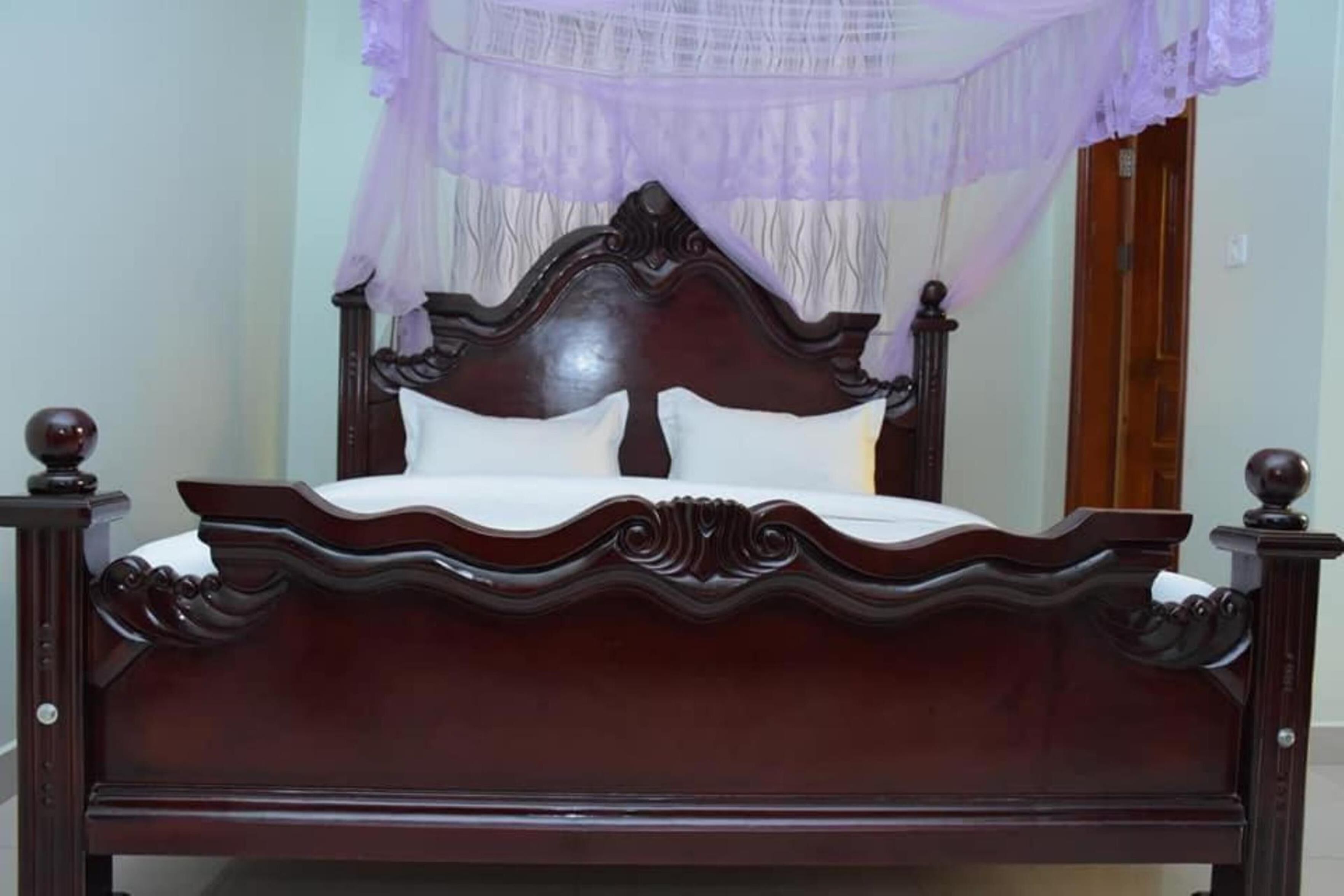 A dark wooden bed with a white mattress and pillows, a decorative headboard, and a purple canopy.