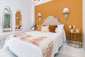 A bedroom with a bed, two wall-mounted lamps, a round table with a plant, and a mirror with a decorative frame.