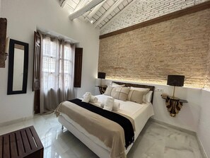 Ein Schlafzimmer mit einem großen Bett, einem Spiegel, einem Fenster mit Vorhängen und einer Ziegelwand.