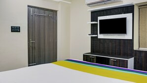 Une chambre avec une armoire, un téléviseur fixé au mur et un lit recouvert d’une couvre-lit aux couleurs vives.