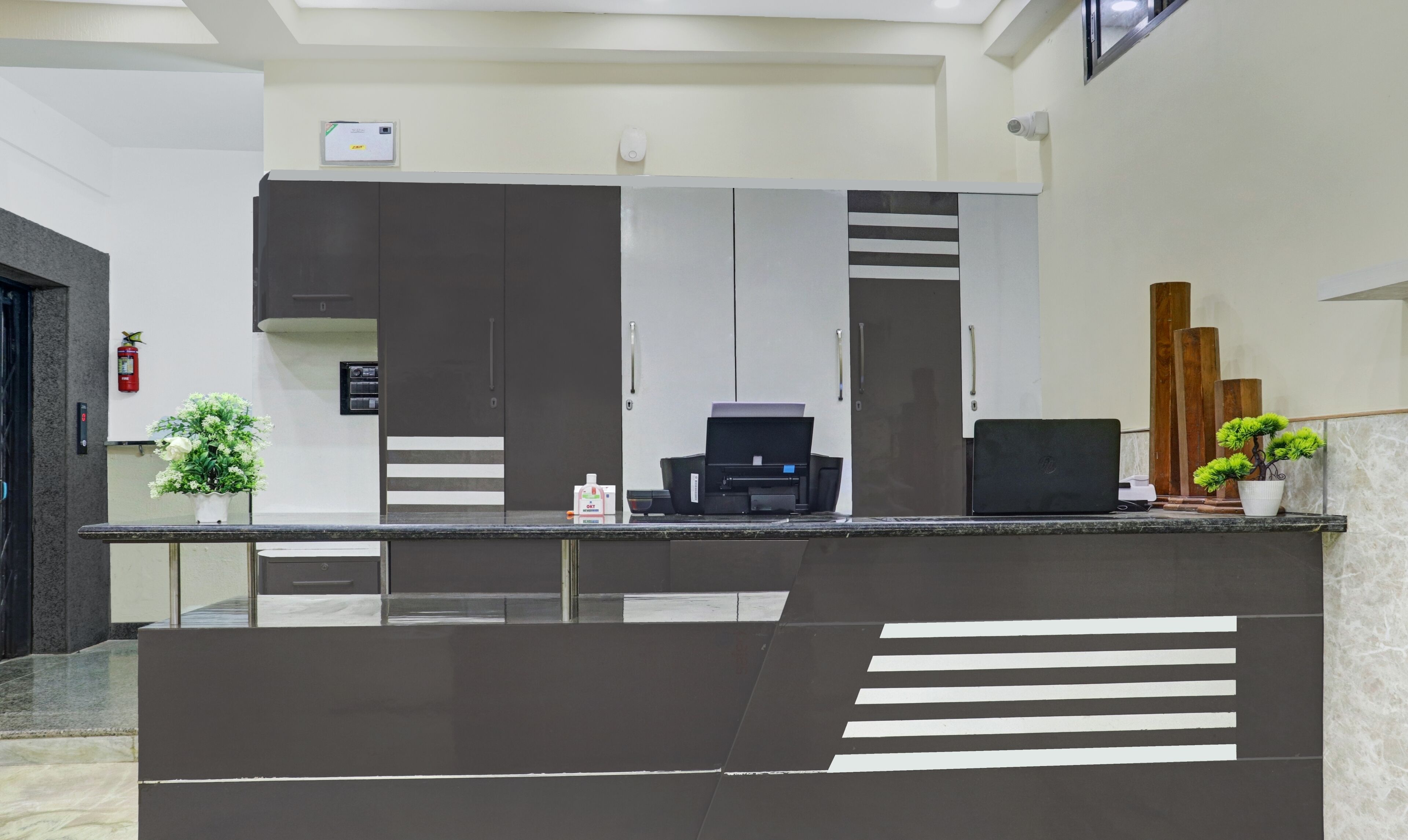 A reception desk with a modern design, a fire extinguisher, a small plant, and a security camera.