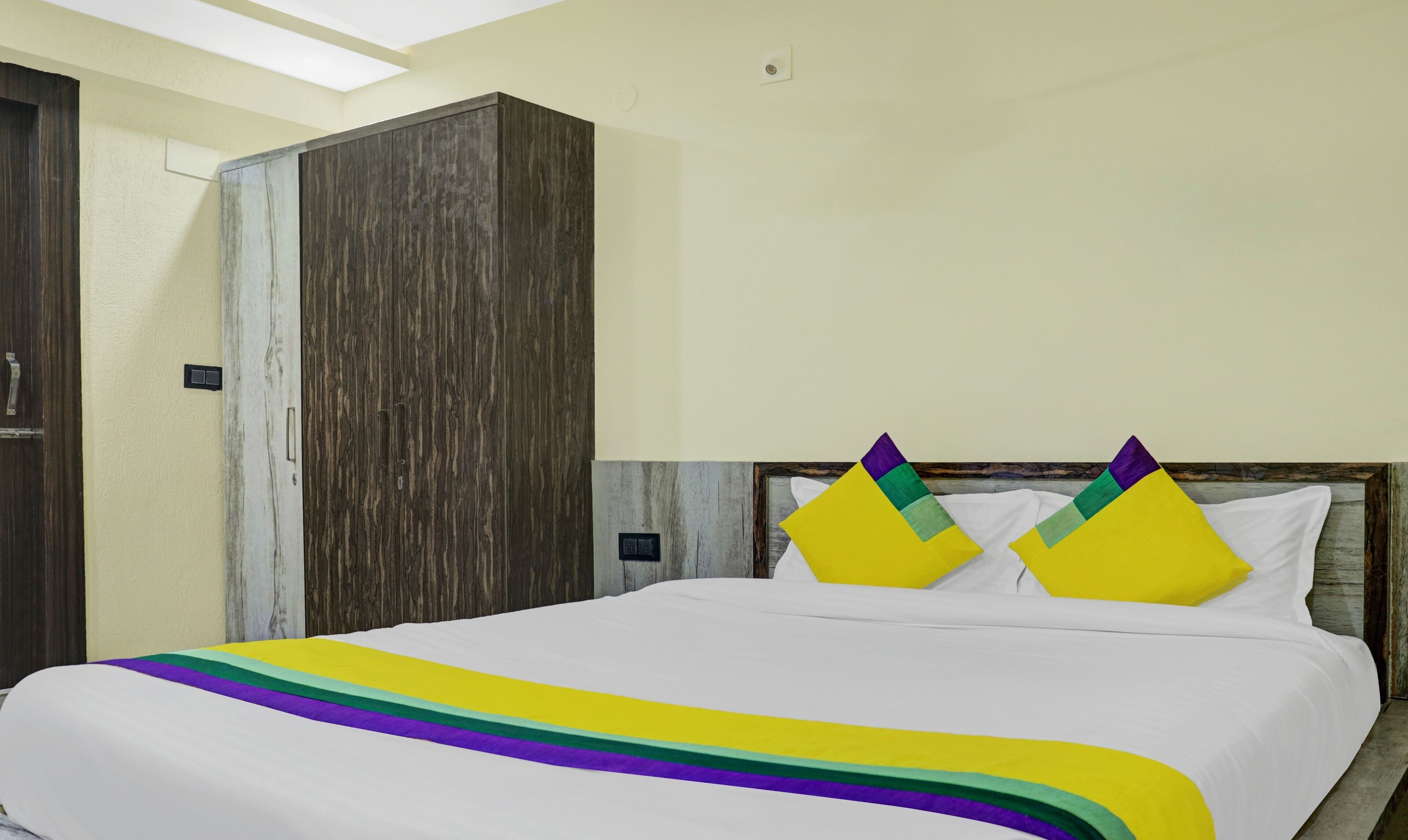 A hotel room with a bed, a wardrobe, and a light-colored wall.