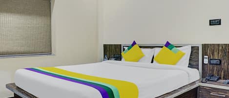 A hotel room with a bed, a nightstand, a phone, and a wall-mounted light switch.