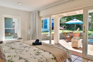 A bedroom with a large bed, a window, and a view of an outdoor patio with a pool and furniture.