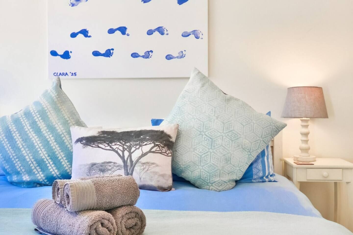A neatly made bed with patterned pillows, a wall art piece, and a bedside lamp.