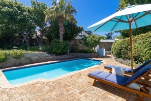 A swimming pool with lounge chairs and an umbrella, surrounded by greenery and stone walls.