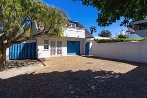 A house with a paved driveway, a blue gate, and a tree in the foreground.