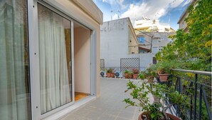Un balcón con macetas, una puerta corrediza de vidrio y vistas a edificios cercanos.