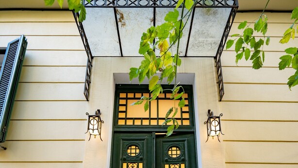 Una puerta doble verde con paneles decorativos, un pequeño tramo de escalones y dos luces fijadas a la pared.