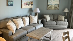 A modern living room with two grey sofas, a wooden coffee table, and a dining table.