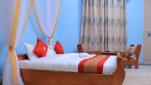 A bedroom with a wooden bed, white bedding, red pillows, a wooden chair, and a table. - Dream Wood Suites (Mbarara)