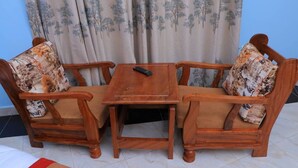A wooden sofa set with floral cushions, a small table, and a remote control on it. - Dream Wood Suites (Mbarara)