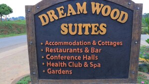 A sign for Dream Wood Suites listing amenities such as accommodation, cottages, restaurants, bars, conference halls, health club, spa, and gardens. - Dream Wood Suites (Mbarara)