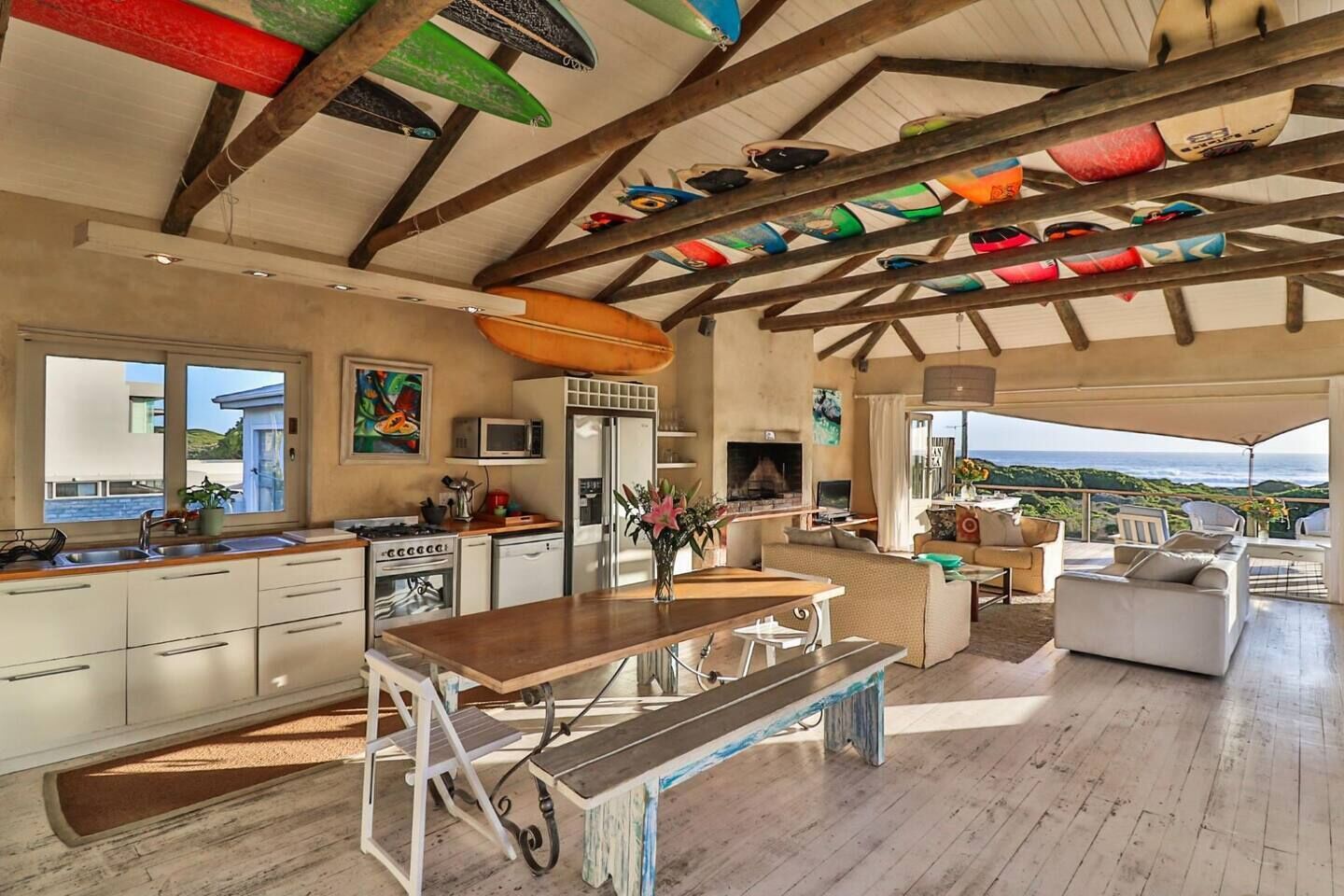 Une cuisine spacieuse équipée d’appareils modernes, un coin repas avec un banc et un salon offrant une vue sur l’océan.