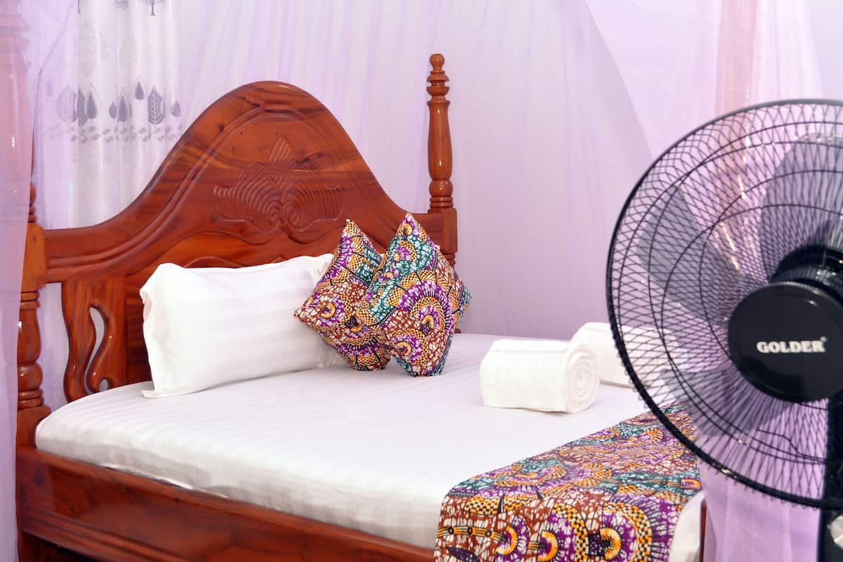 Una cama de madera con ropa de cama blanca, una almohada estampada y un abanico negro.