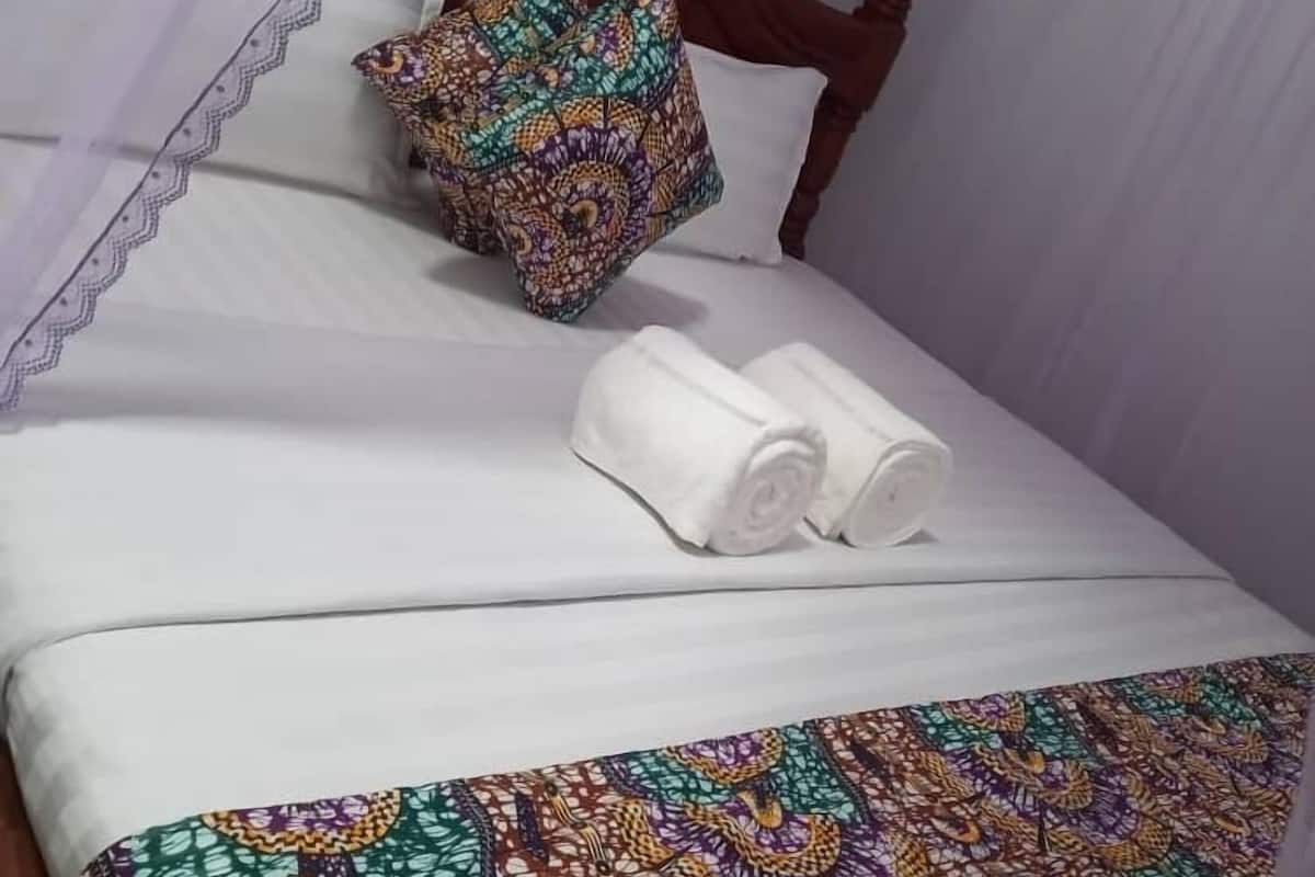 Una cama bien hecha con una colcha estampada y colorida, una almohada decorativa y toallas blancas enrolladas.