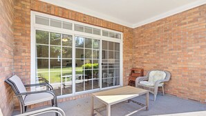 A covered patio area with a brick wall, a large sliding glass door, and outdoor furniture including chairs and a table. - 813 Cypress Bend - Barefoot Resort Rentals (North Myrtle Beach)
