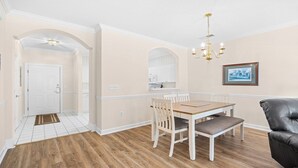 A dining area with a wooden table and chairs, a black leather chair, and a chandelier. - 813 Cypress Bend - Barefoot Resort Rentals (North Myrtle Beach)