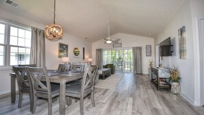 Un vaste espace dédié à la salle à manger, avec une table et des chaises en bois, un ventilateur de plafond et une vue sur l’extérieur.