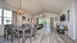 A spacious dining area with a wooden table and chairs, a ceiling fan, and a view to the outside.