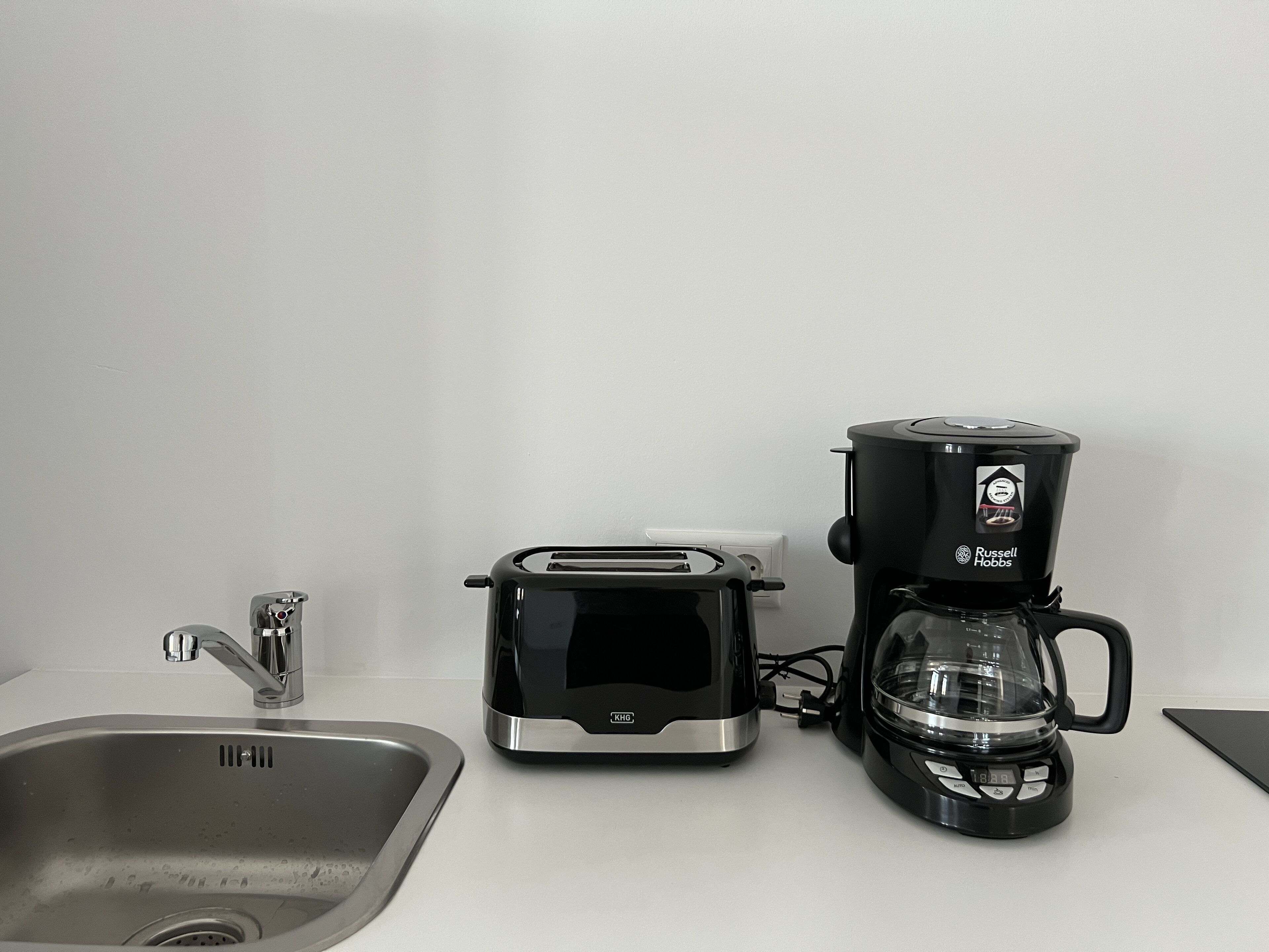 Une cuisine équipée d’un évier en acier inoxydable, d’un grille-pain et d’une machine à café posés sur le plan de travail.