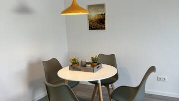 A dining area with a round table, four chairs, a pendant light, and a framed picture on the wall.