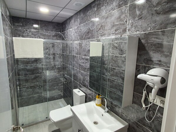 A modern bathroom with a glass-enclosed shower, a white sink, and a hairdryer on the wall. - Özturks Hotel  (Istanbul)