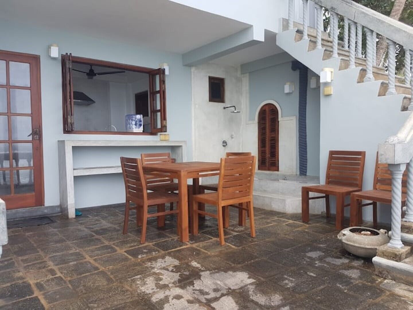 Un coin repas avec une table et des chaises, une fenêtre avec un rideau et un escalier doté d’une balustrade.