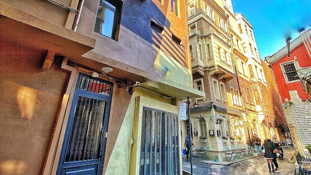 A street view with multi-story buildings, a gated entrance, and a clear blue sky. - Nomad Hostel Karakoy (Istanbul)