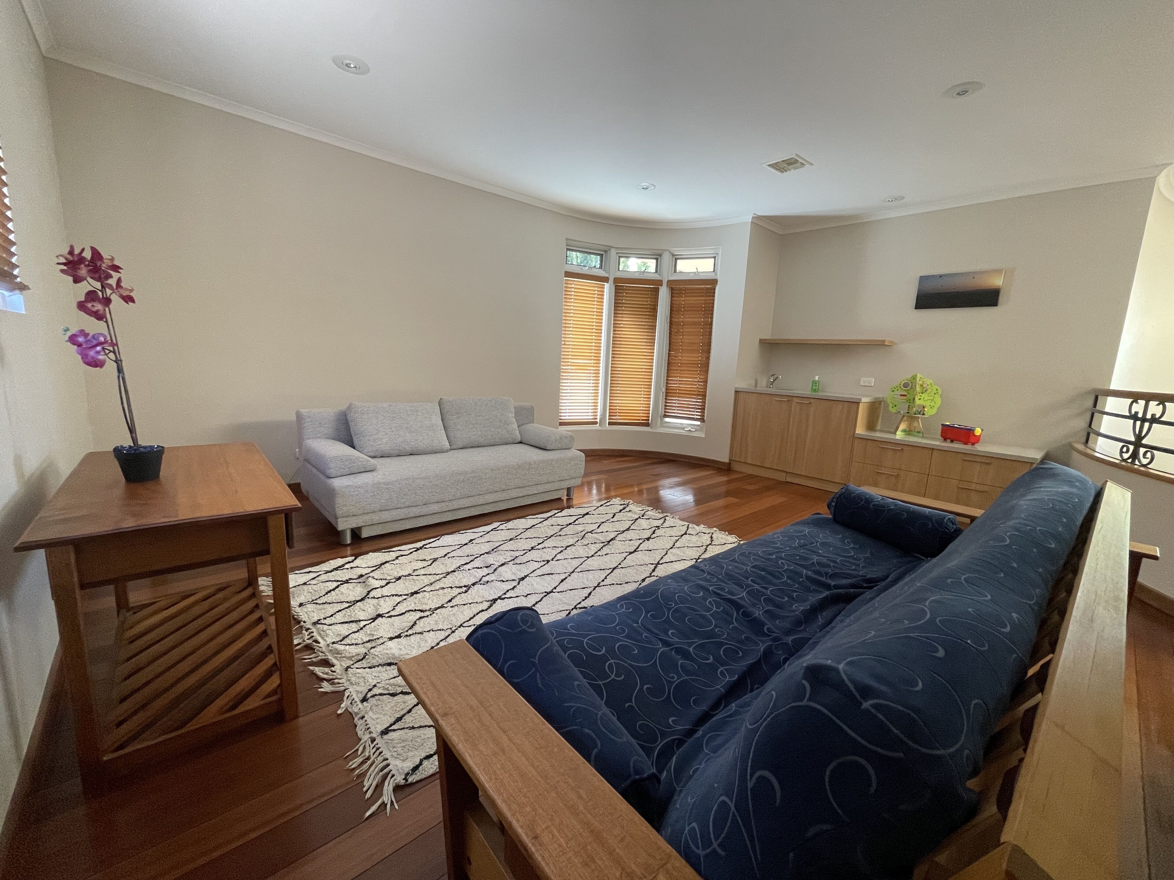 A living room with a sofa, a coffee table, a small table with a plant, and a kitchen area in the background.