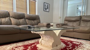 Ein Wohnzimmer mit einem Glastisch, zwei braunen Ledersofas und einem Teppich in Rot und Beige.