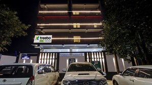 A multi-story building with a 'treebo' sign, parking area, and cars. - Treebo Noida Grand (Noida)