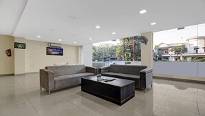 A spacious lobby with a grey sofa set, a coffee table, and a large window offering a view of the outside. - Treebo Noida Grand (Noida)