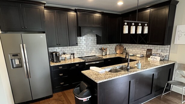 Cocina moderna con armarios oscuros, refrigerador de acero inoxidable, encimera de granito y un cubo de basura negro.