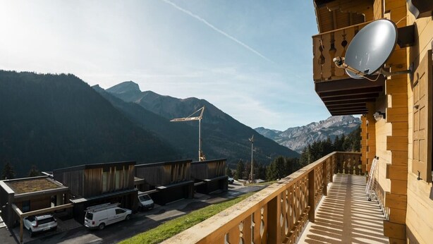 Un balcon avec vue sur les montagnes, une antenne parabolique et des véhicules garés.