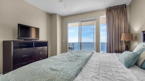 Quarto de hotel com uma cama, uma televisão num móvel de madeira, varanda com cortinas e vista para o mar.