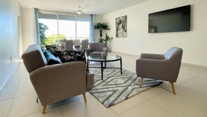 Ein modernes Wohnzimmer mit einer Couch, zwei Sesseln, einem Couchtisch und einem an der Wand befestigten Fernseher.