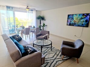 A modern living room with a sofa, armchairs, a coffee table, and a TV mounted on the wall.