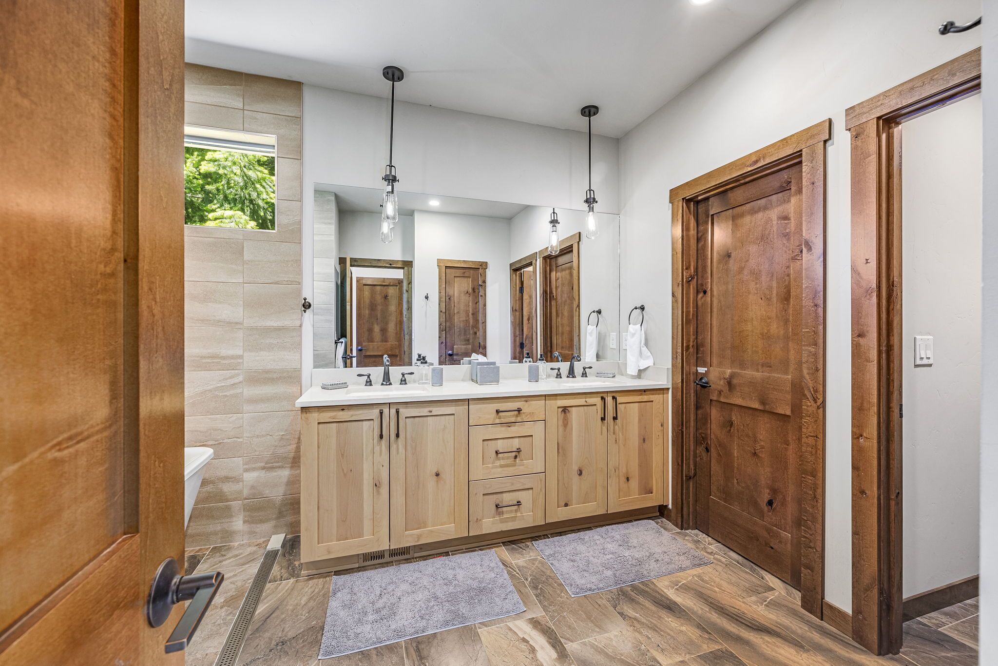 Une salle de bain moderne avec des meubles en bois, un grand miroir et des luminaires suspendus.