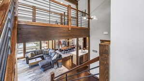 A spacious loft-style living area with a mezzanine, wooden beams, and a large window overlooking a patio. - Family-Friendly Luxury | Great Amenities + 1PM Check-In & Check-Out (Cle Elum)