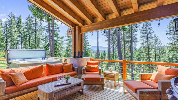 A wooden deck with wicker furniture, a hot tub, and a view of a forest. - Family-Friendly Luxury | Great Amenities + 1PM Check-In & Check-Out (Cle Elum)