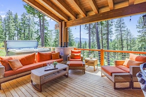 Une terrasse en bois avec des meubles en osier, un jacuzzi et une vue sur une forêt.