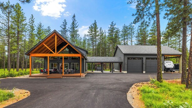 Une cabane dotée d’un porche abrité, d’un garage et d’une allée bordée d’arbres.