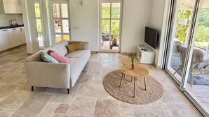 Ein geräumiges Wohnzimmer mit einer Couch, einem Couchtisch und einem Fernseher. Eine Glastür führt in einen Außenbereich.