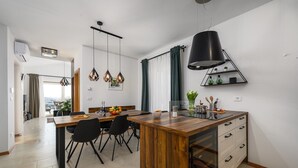 Eine moderne Küche mit einer Holzinsel, schwarzen Stühlen, Pendelleuchten und einem Einbauofen.