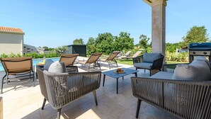 Eine Terrasse im Freien mit Korbmöbeln, einem Grill und einem Pool im Hintergrund.