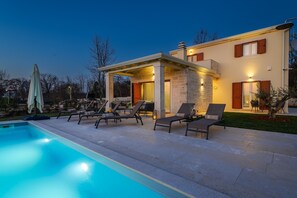 Un espace piscine extérieur moderne, doté de chaises longues et d’un coin salon abrité.