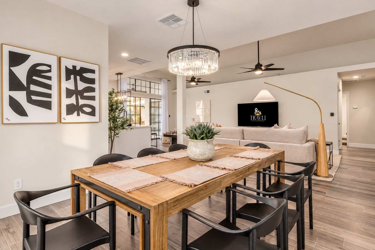 A modern dining area with a wooden table, black chairs, and a chandelier.